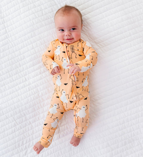 Baby wearing an orange -colored onesie with halloween prints on a white textured surface