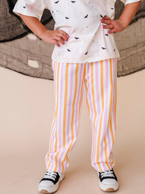 Child wearing a white top with halloween patterns and striped pants on a beige background