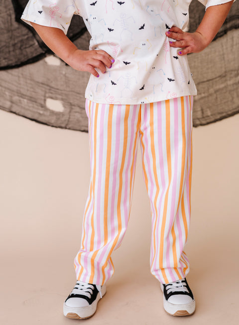 Girl wearing a cream top with black patterns and striped pants on a beige background