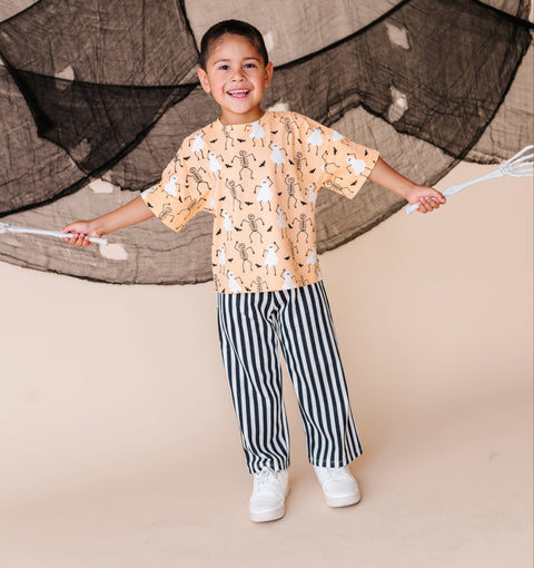 Child wearing a patterned shirt and striped pants standing in front of a netted backdrop.