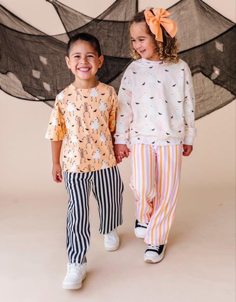 Two children holding hands in front of a decorative net, wearing patterned outfits.