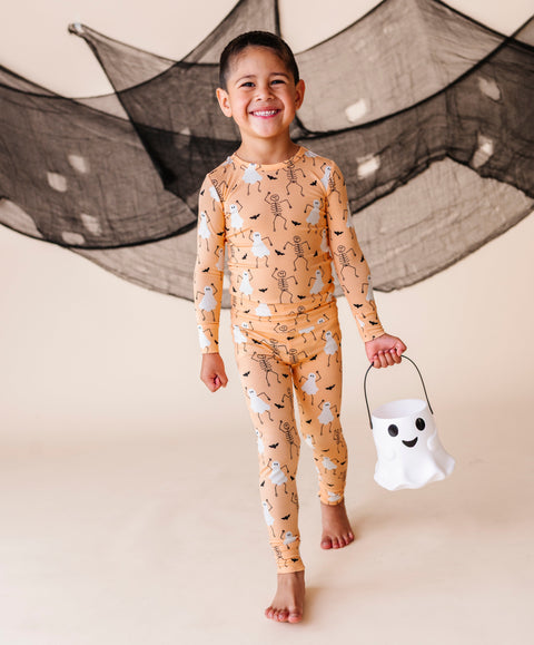 Child wearing Halloween-themed pajamas holding a ghost candy bucket with a decorative net in the background.