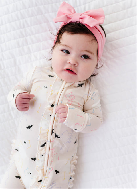 Baby wearing a pink headband and white onesie with black bat patterns on a white blanket.