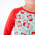 Children's pajama top with red sleeves and festive hot chocolate pattern on a light blue background