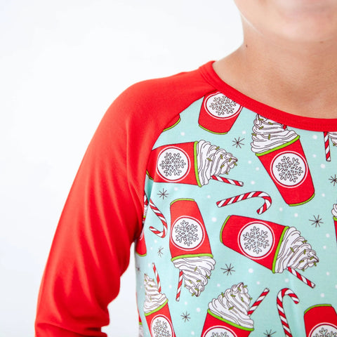 Children's pajama top with red sleeves and festive hot chocolate pattern on a light blue background
