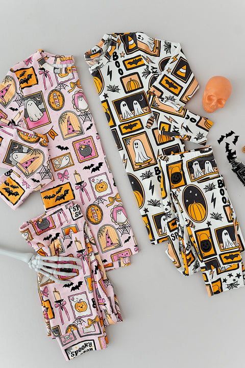 Two children's pajama sets laid flat on a light gray background. One set is light pink with a Halloween-themed print featuring ghosts, pumpkins, bats, and haunted houses.
